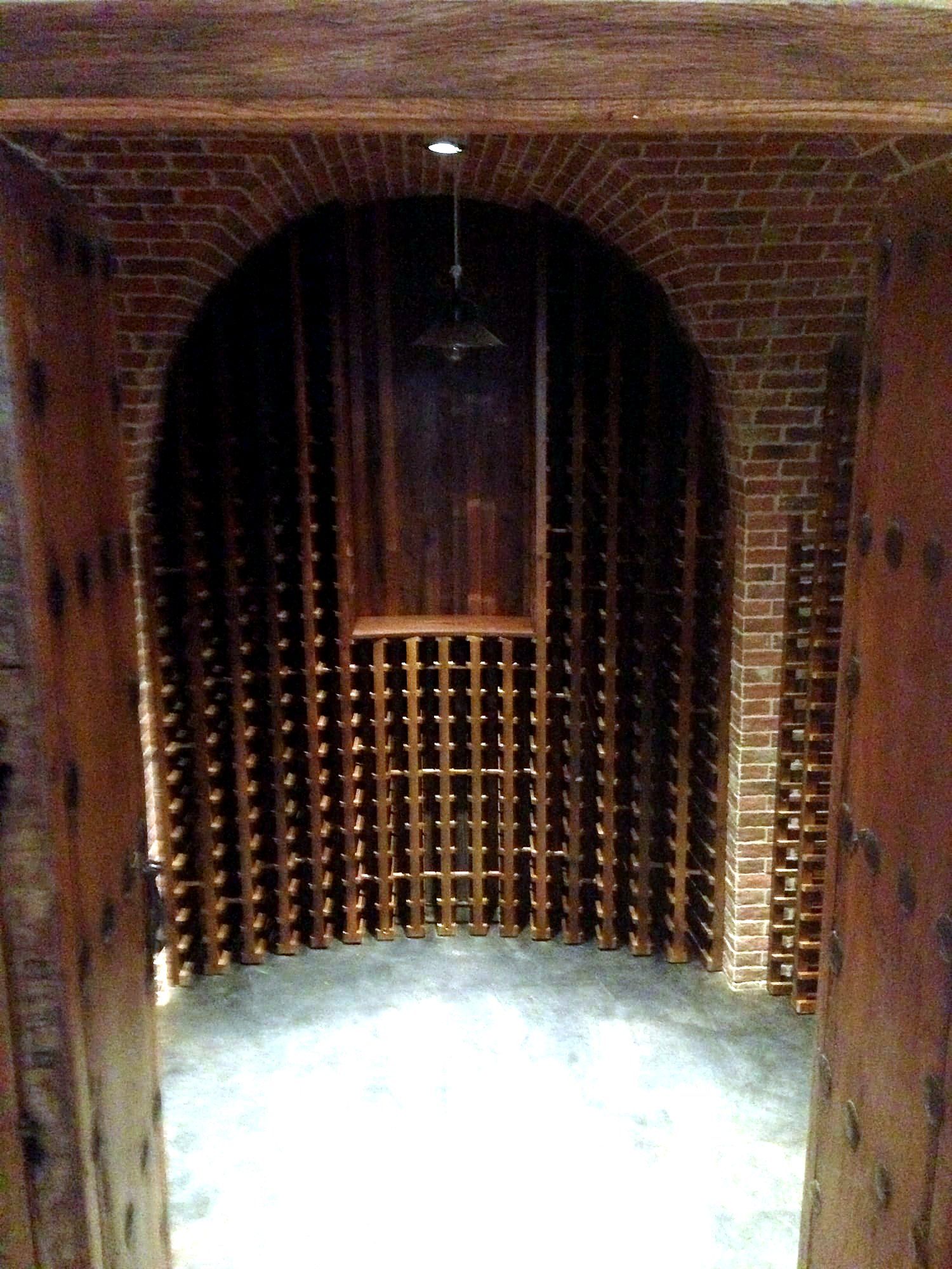 Arched brick-lined wine cellar with dark wood wine racks lining both walls to a tasting nook