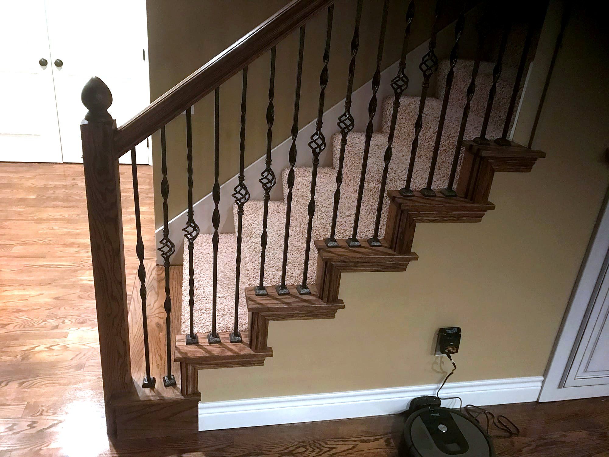 Staircase with wrought iron spindles, a dark wood handrail, and oak treads