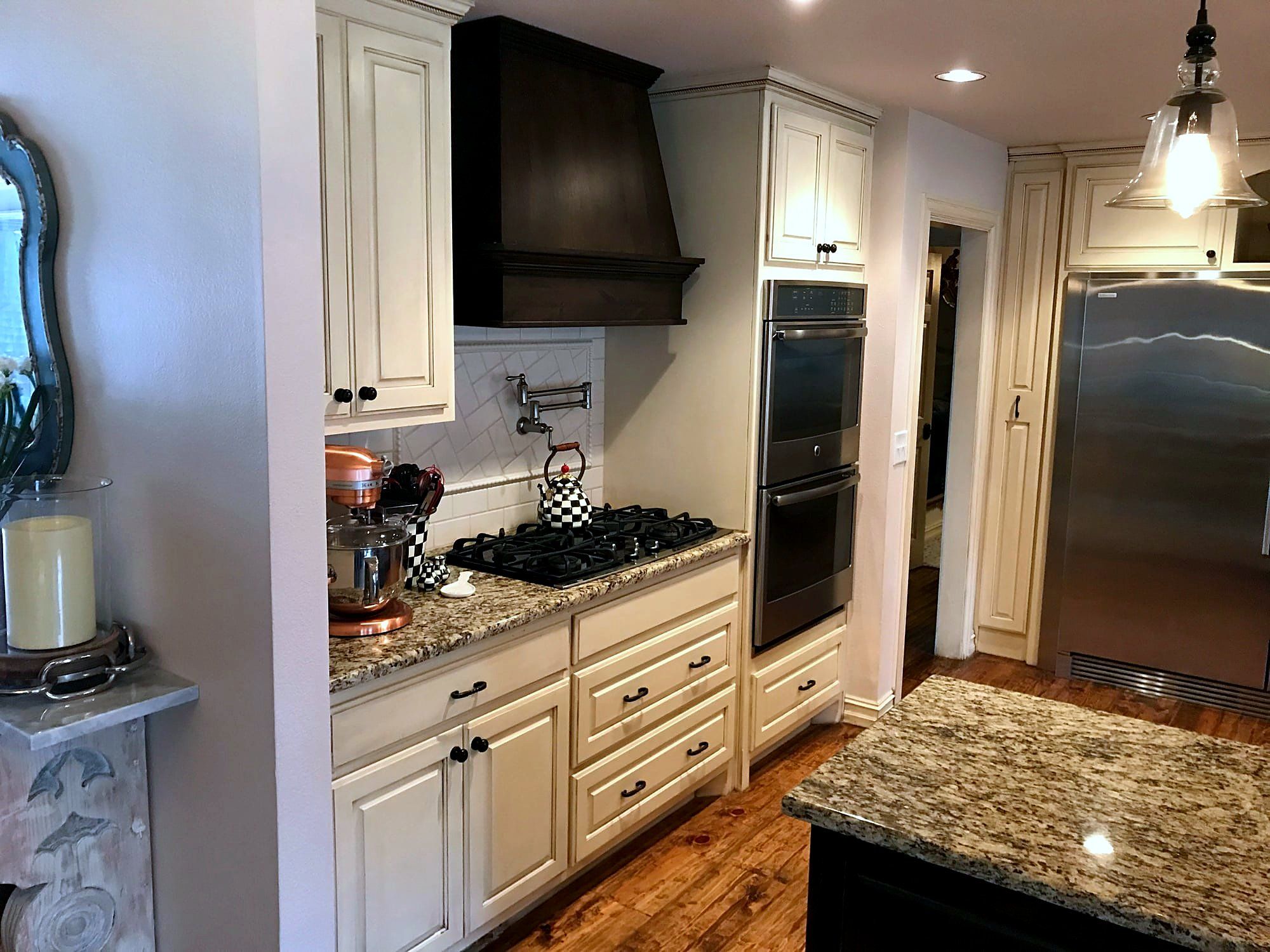 Cream kitchen cabinetry with a dark wood vent hood, built-in double ovens, and granite countertops