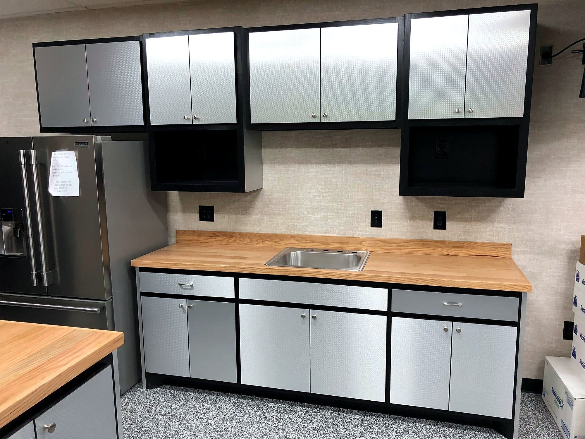 Garage cabinetry with laminate doors and a wood countertop beside a stainless refrigerator