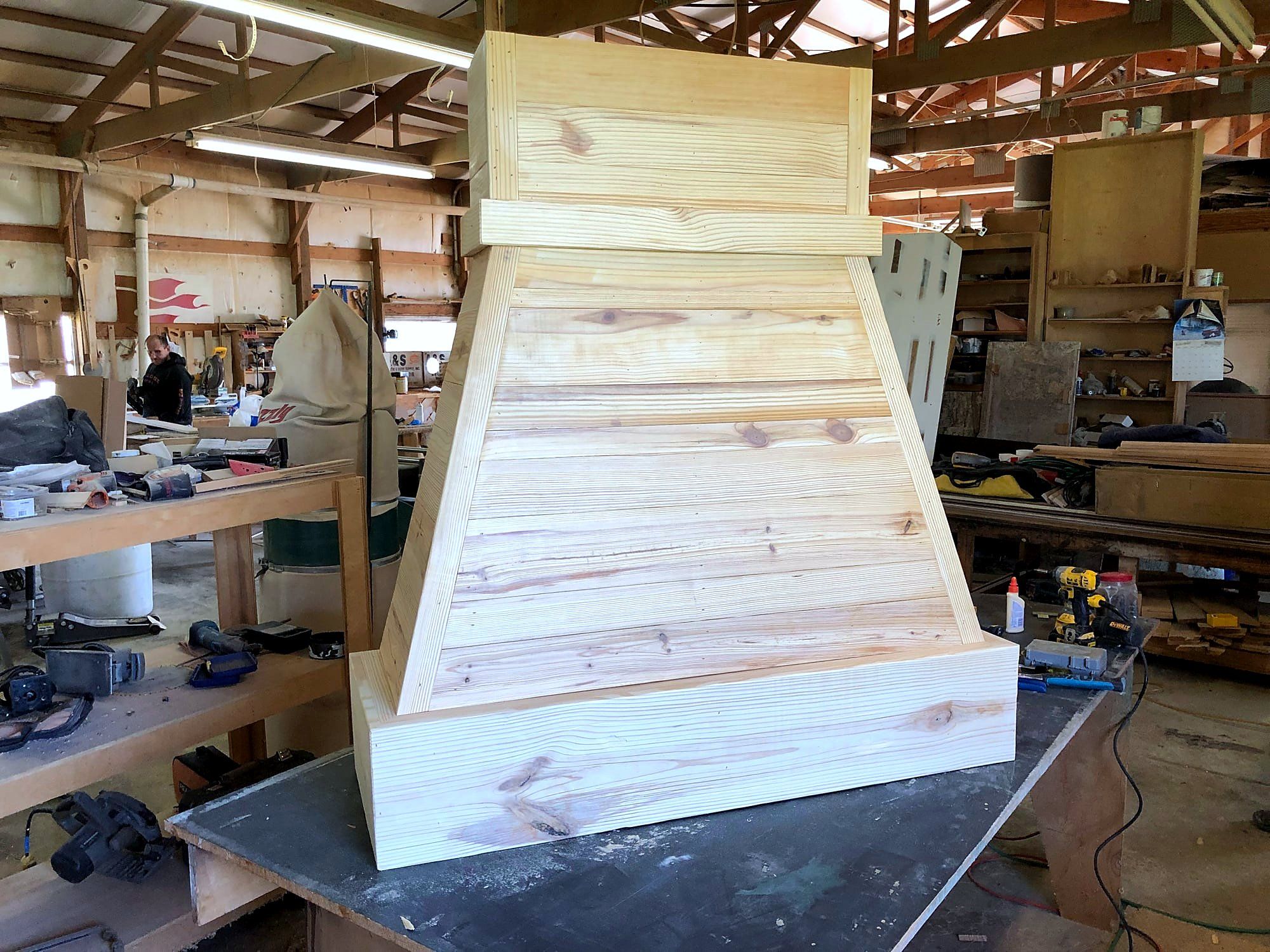 Tapered range hood cabinet in cross-grain pine board, corbel-shaped base, under construction on a shop workbench