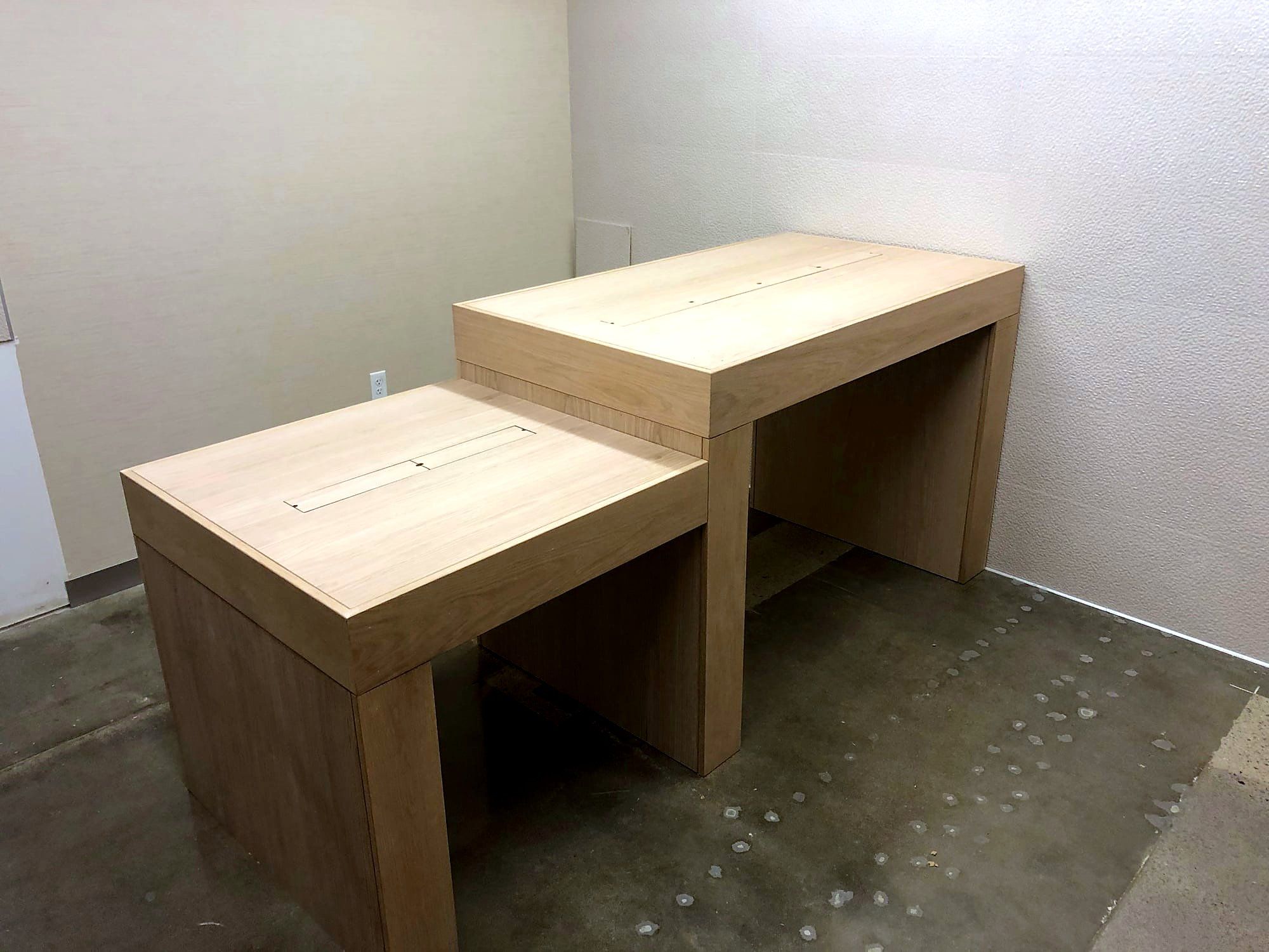 Two-tier wood desk with a cable pass-through slot in an otherwise empty room