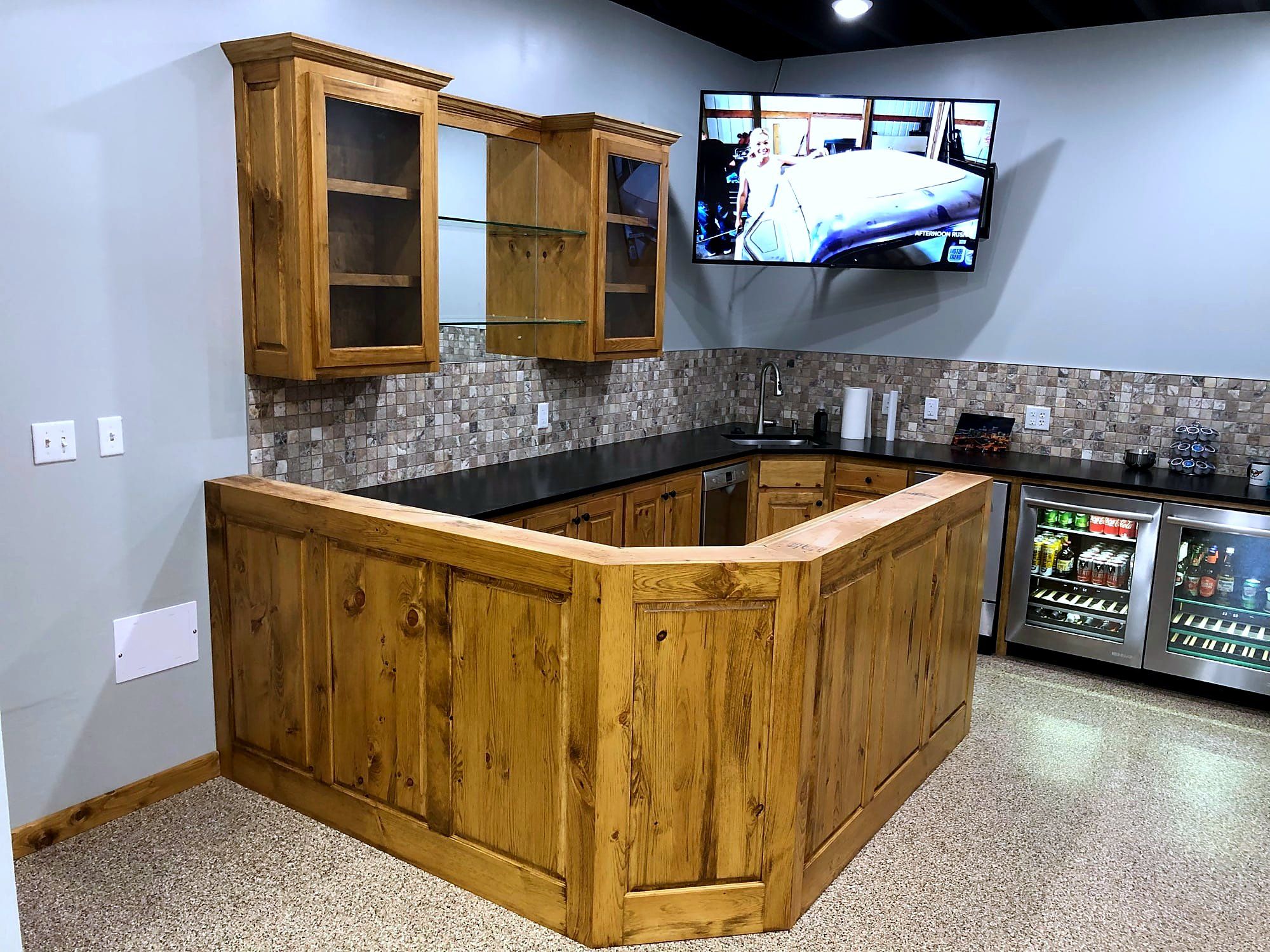 Finished wet bar with glass-front cabinets, granite counters, a mini fridge, and a mounted television