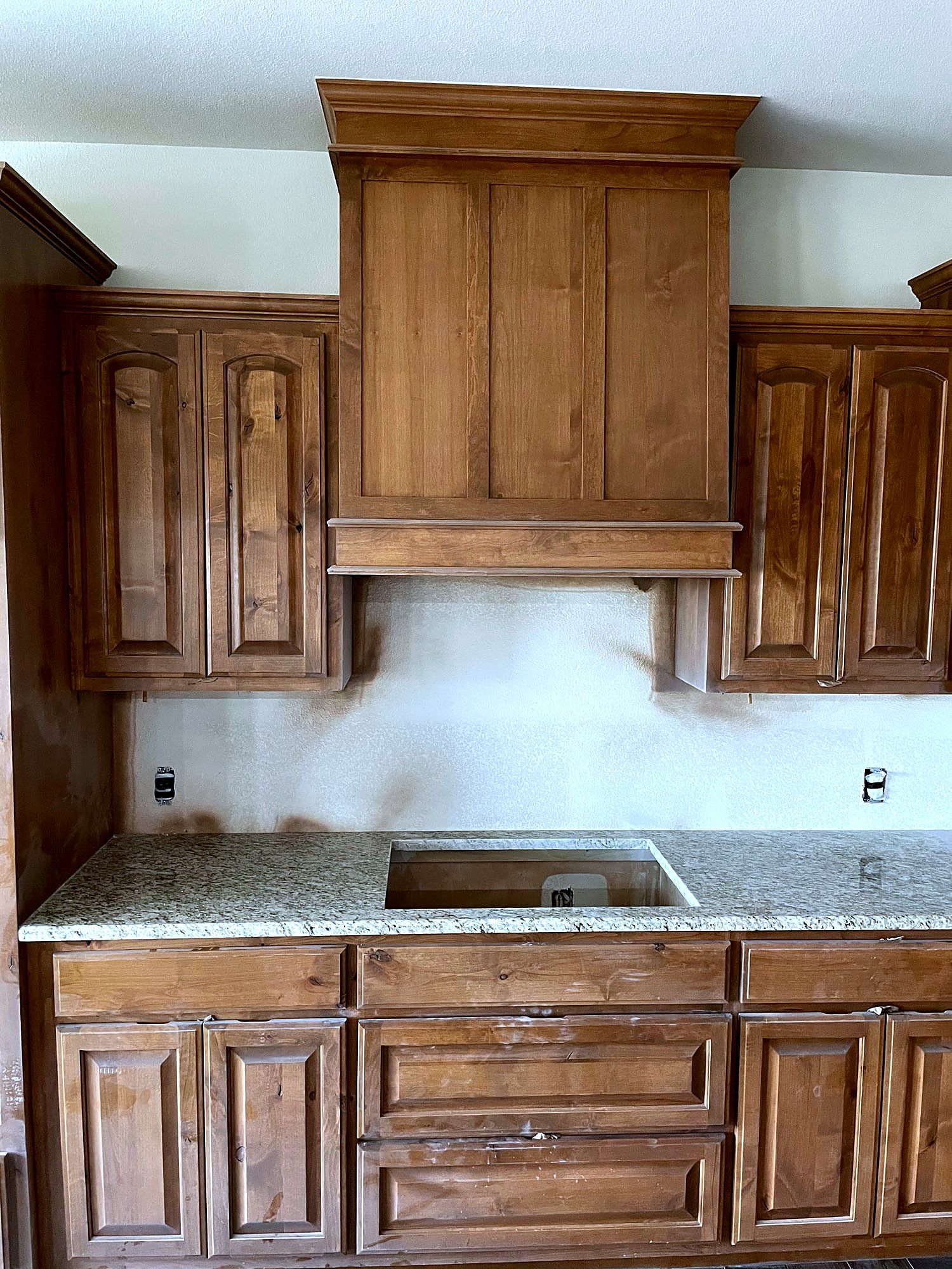 Stained wood kitchen hood cabinet with raised-panel doors and a granite countertop