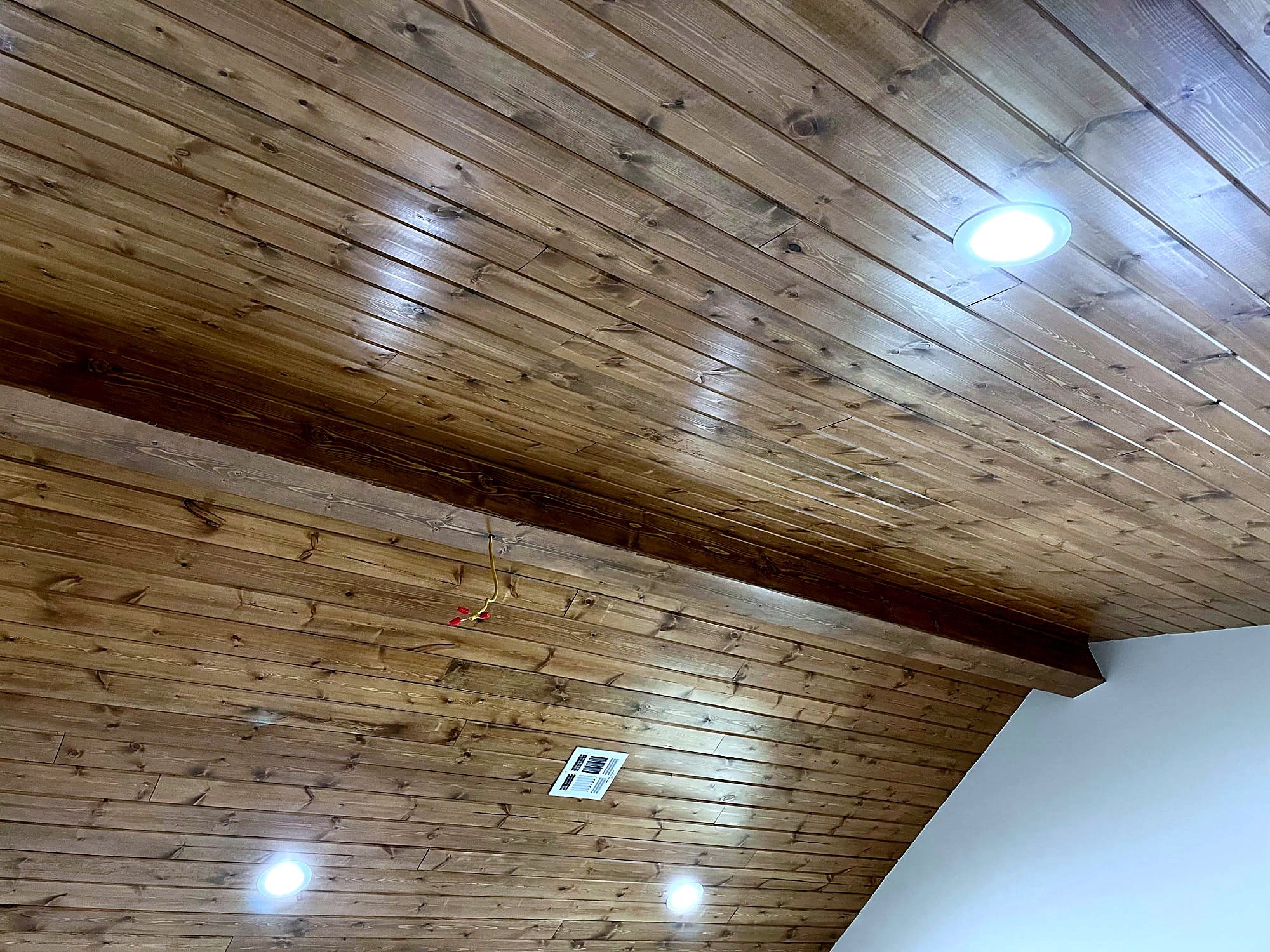 Tongue-and-groove wood plank ceiling with an exposed beam and recessed lighting