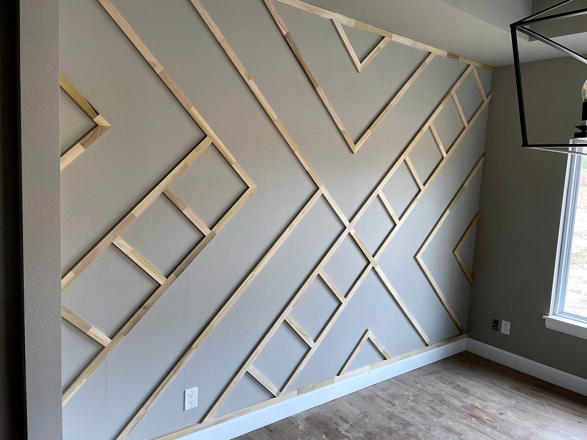 Geometric chevron accent wall built from mitered wood strips in a repeating diamond and triangle pattern, floor to ceiling