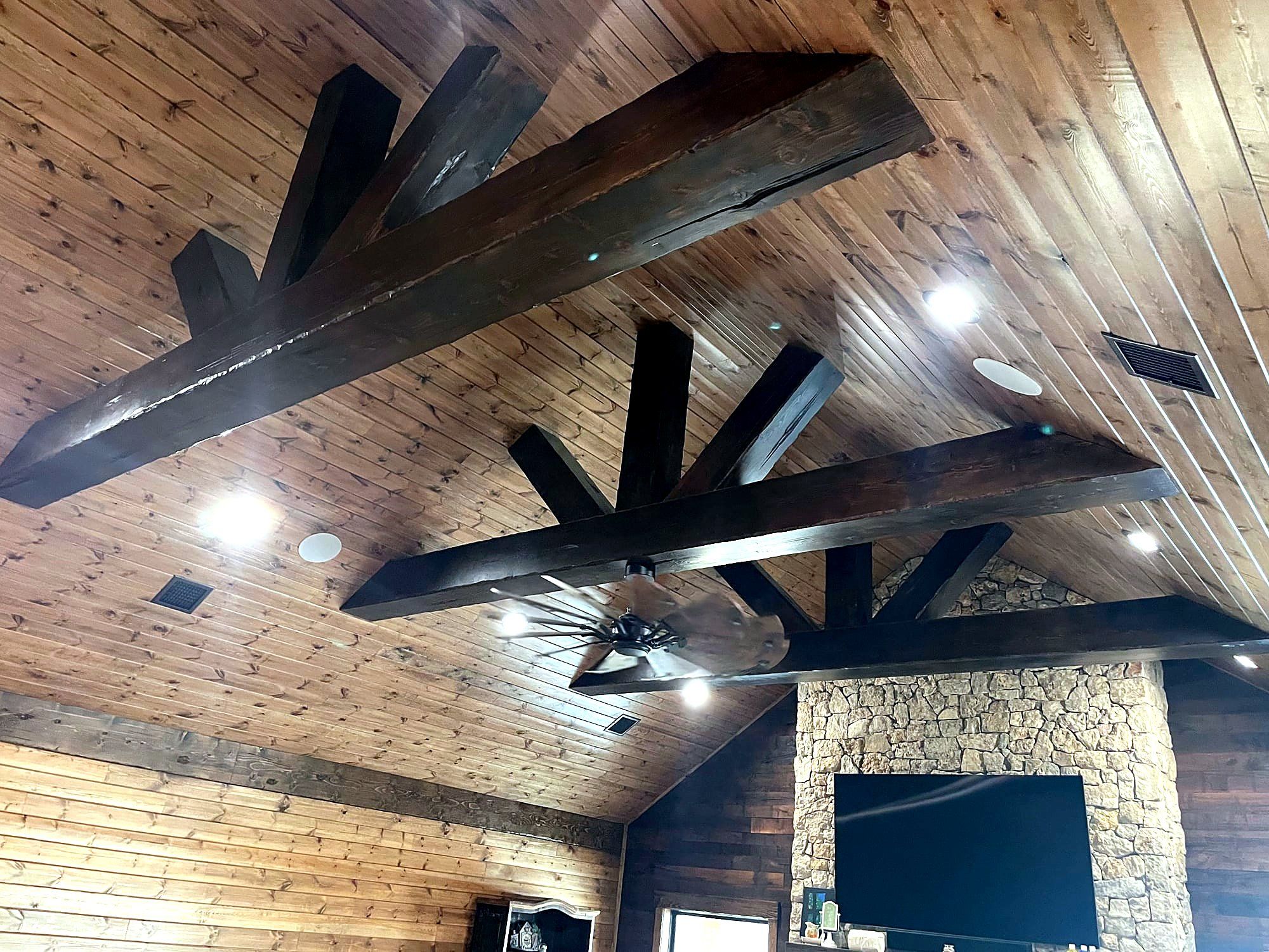 Great room with a dark stained beam ceiling, tongue-and-groove planking, and a stone fireplace