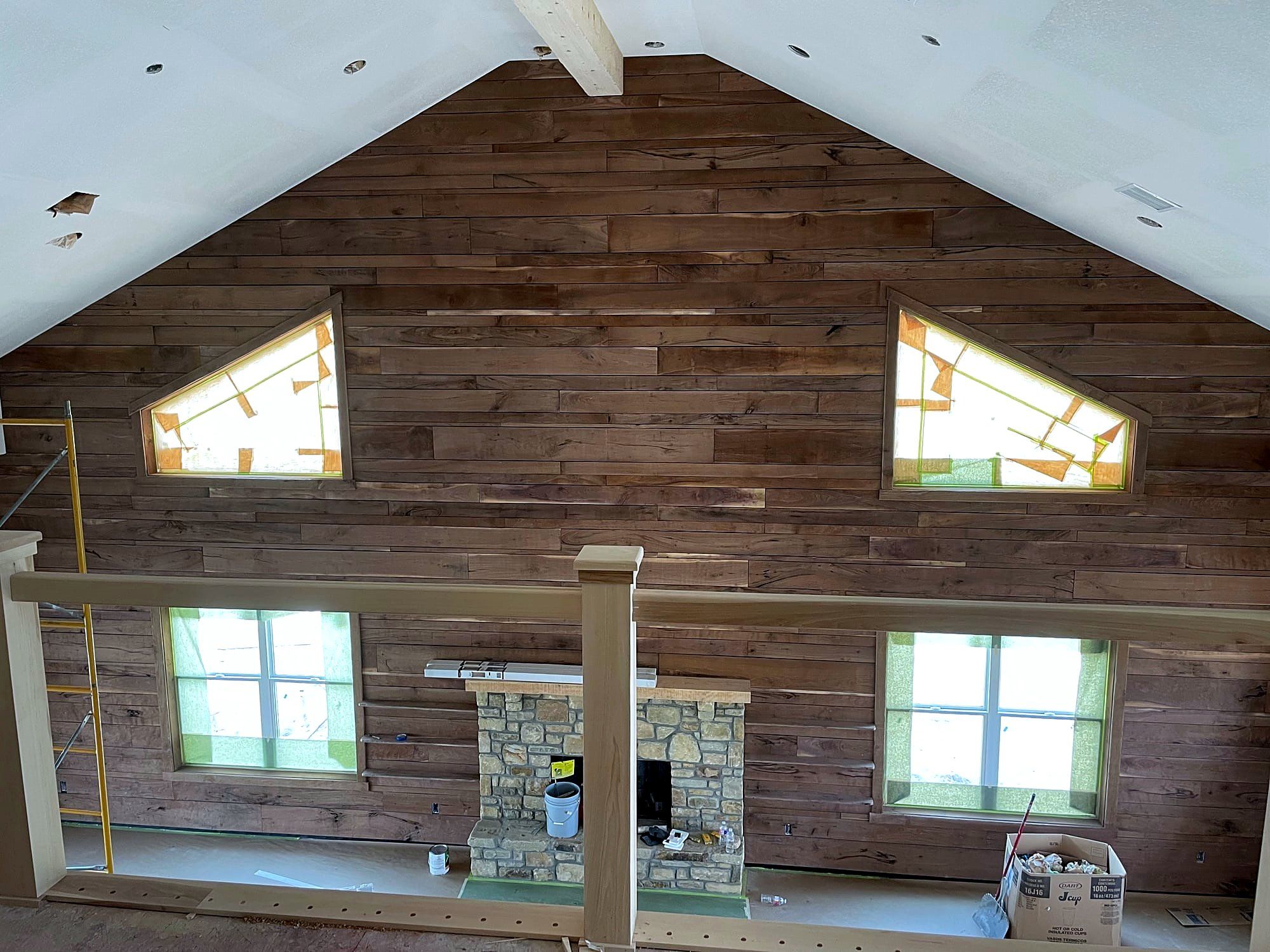 Great room with a stained wood plank accent wall, a stone fireplace, and triangular windows