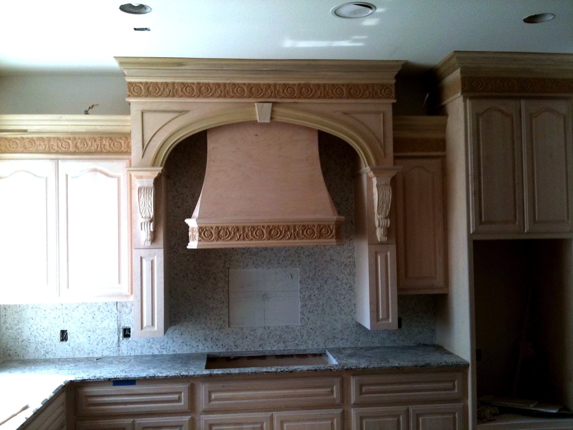Kitchen range hood cabinet with carved corbels and ornate crown molding above granite counters