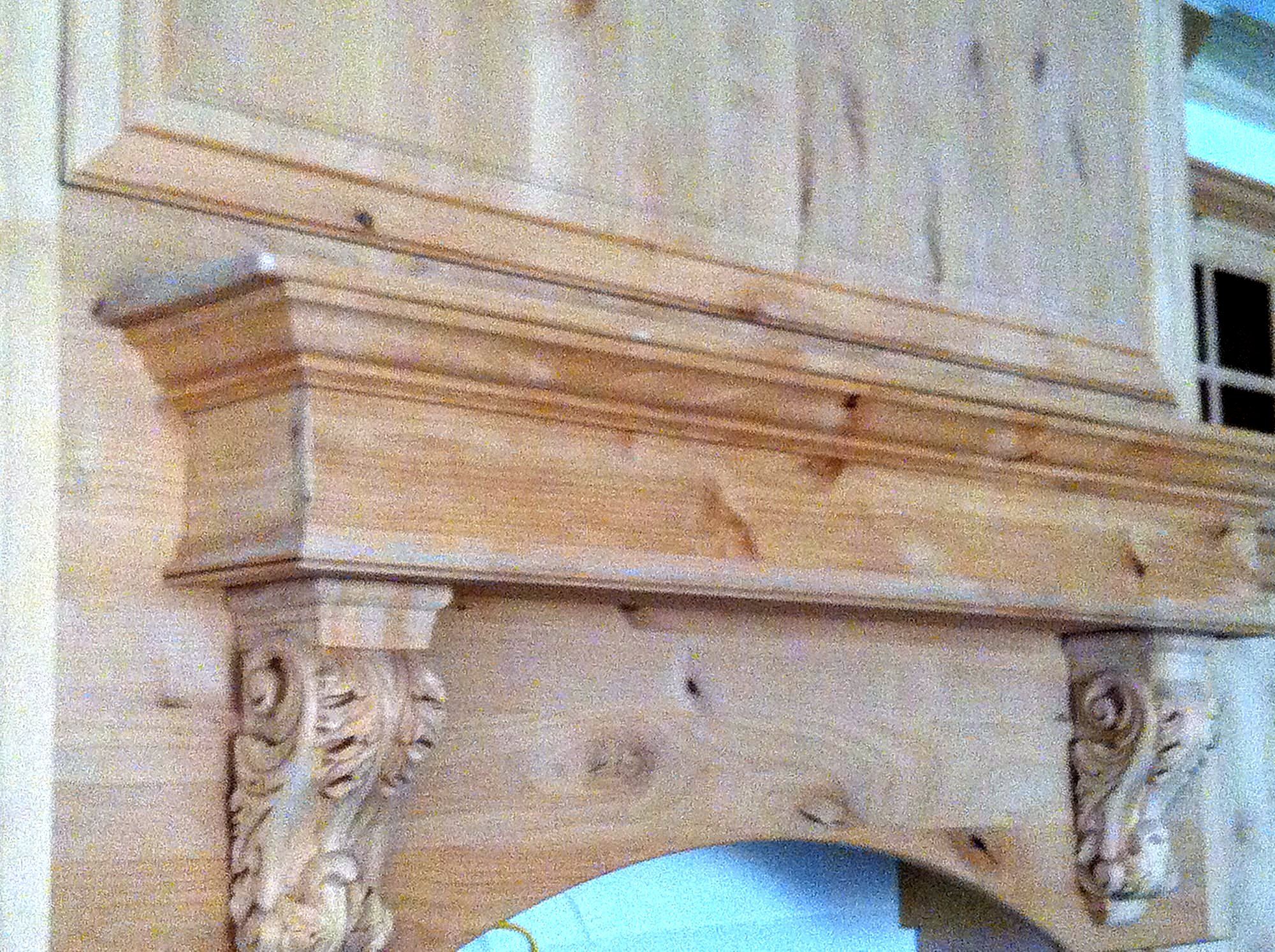 Close view of a pine mantel shelf with carved acanthus-leaf corbels beneath a bold crown